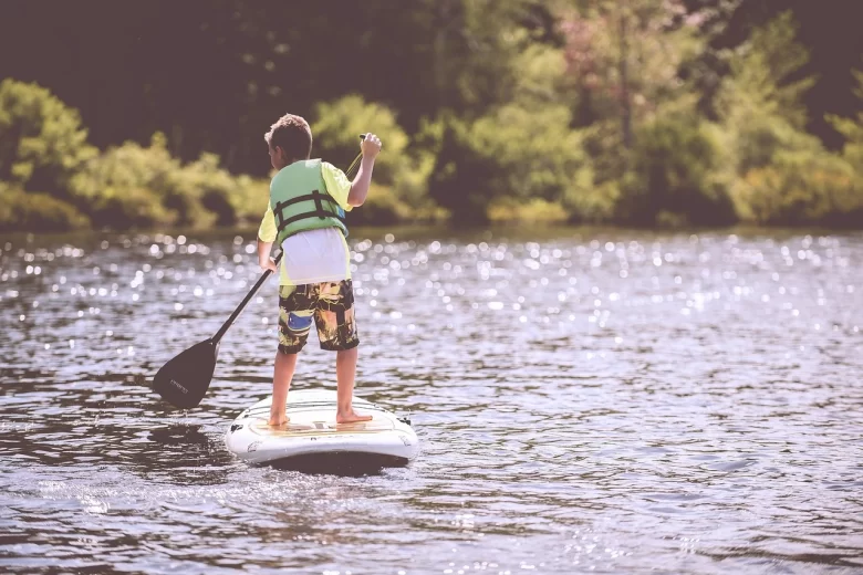 Pai e filho praticando canoagem com crianças em um lago de águas claras, ambos usando coletes salva-vidas.