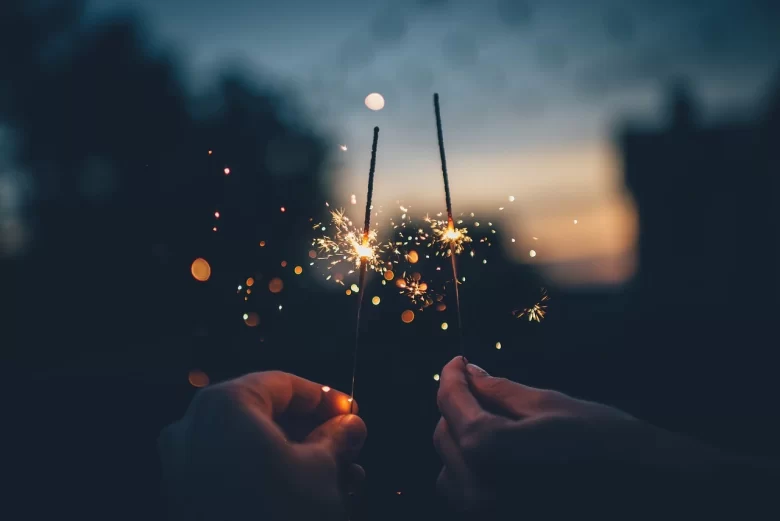 Mãos de uma família segurando velas faísca (sparklers) durante uma celebração de Réveillon tranquilo com crianças.